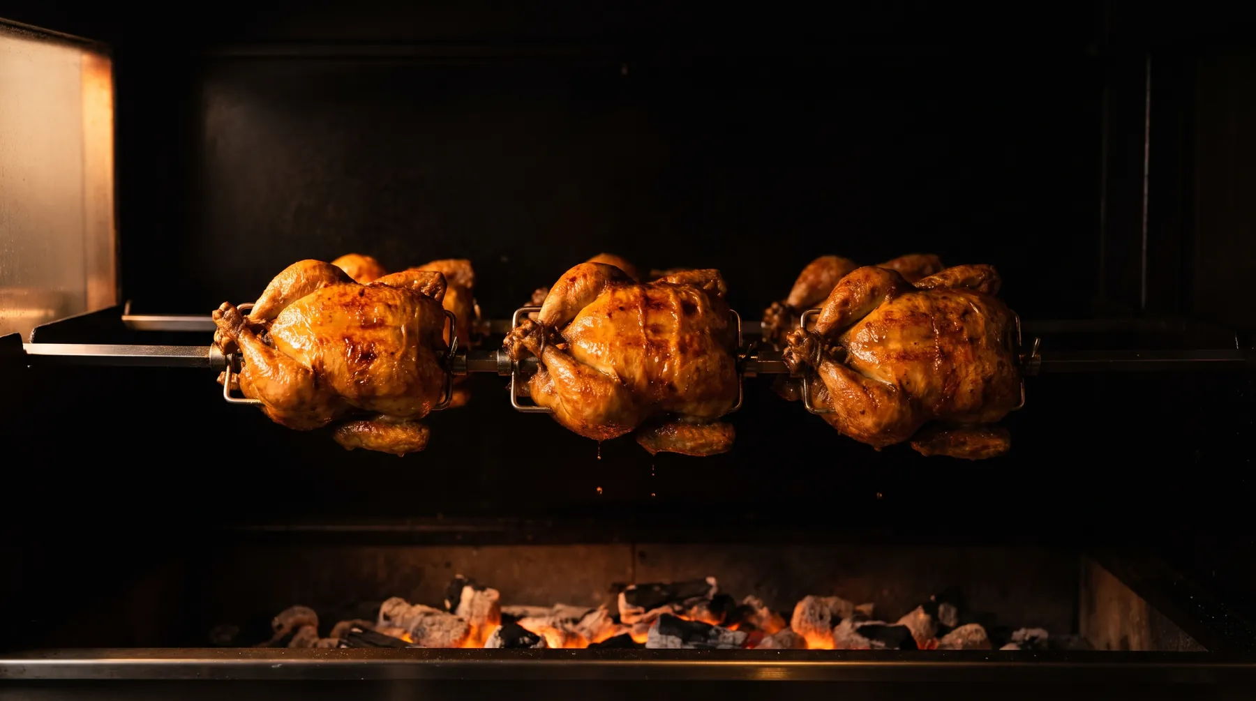 Des poulets entiers qui dorent sur les broches de la rôtissoire, au-dessus des braises rougeoyantes